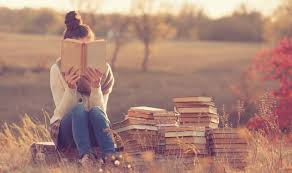 reading teen girl in field of grass with books next to her